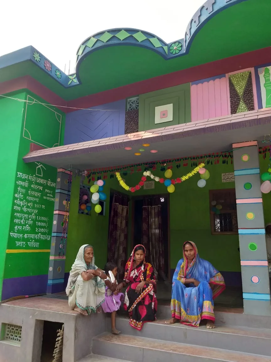 Women beneficiaries outside a decorated PMAY-G home